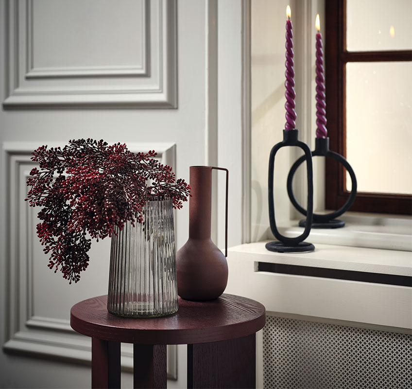 Váza s červenou umelou rastlinou na bordovom červenom stolíku
