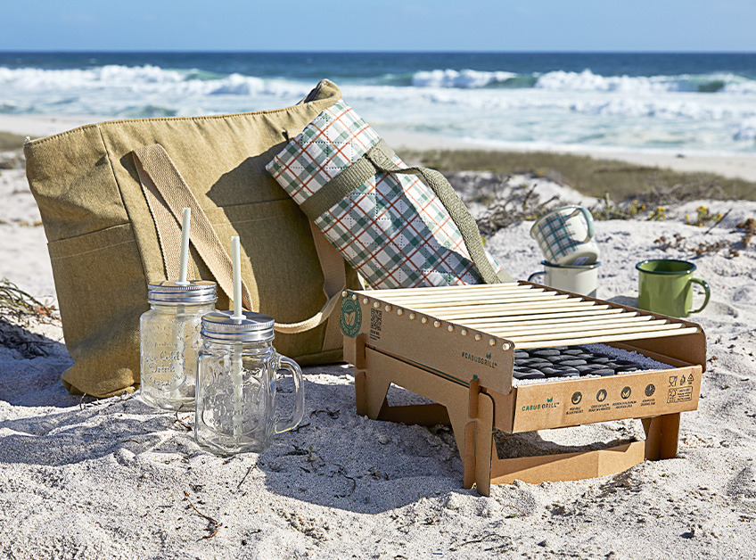Jednorazový gril, poháre a hrnčeky na pitie položené na piesku na pláži