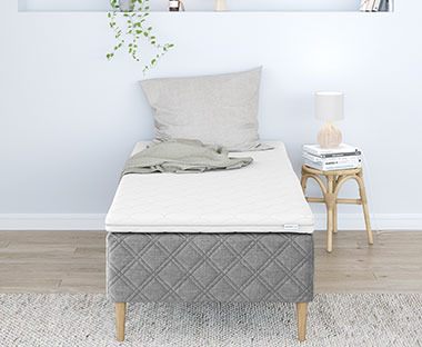 Biely matrac na sivom posteľovom ráme so sivým ozdobným vankúšom