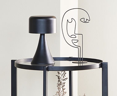 Čierna lampa na stolíku a kovová dekorácia