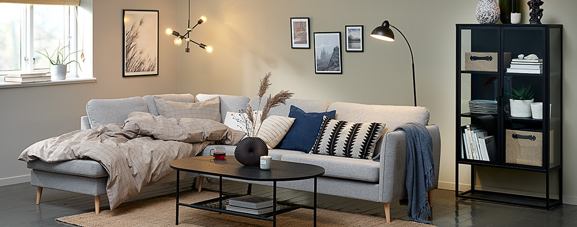 Hygge v obývacej izbe s veľkou rohovou pohovkou, paplónom, vankúšmi a osvetlením.