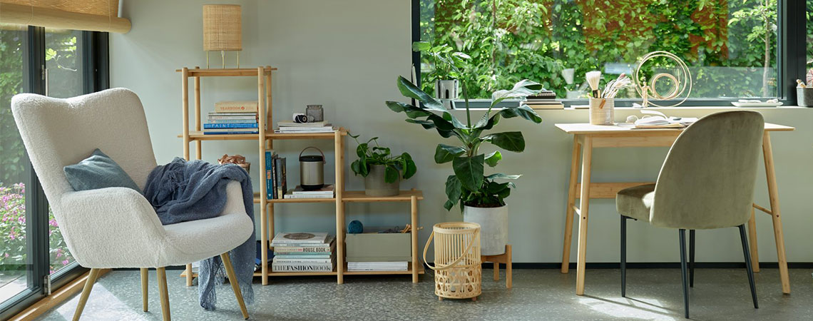 Sivé kreslo pri okno a bambusový regál v pozadí. Bambusový lampáš na podlahe vedľa bambusového stola a olivovo zelenej jedálenskej stoličke