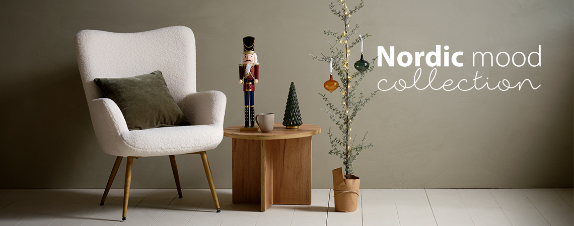 Kreslo s dekoračným vankúšom, konferenčným stolík s vianočnými figúrkami a úzky vianočný stromček so sklenenými vianočnými ozdobami