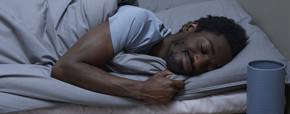 Muž spiaci na posteli zakrytý sivým paplónom