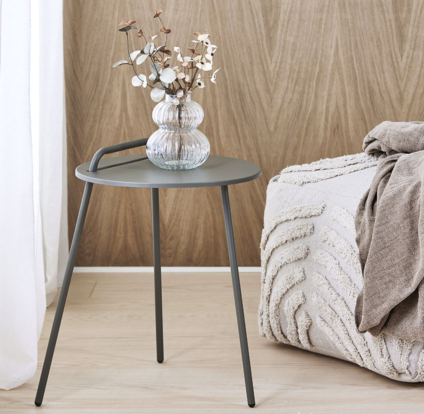 Minimalistic end table with three legs and handle and light beige pouffe with soft, patterned surface 