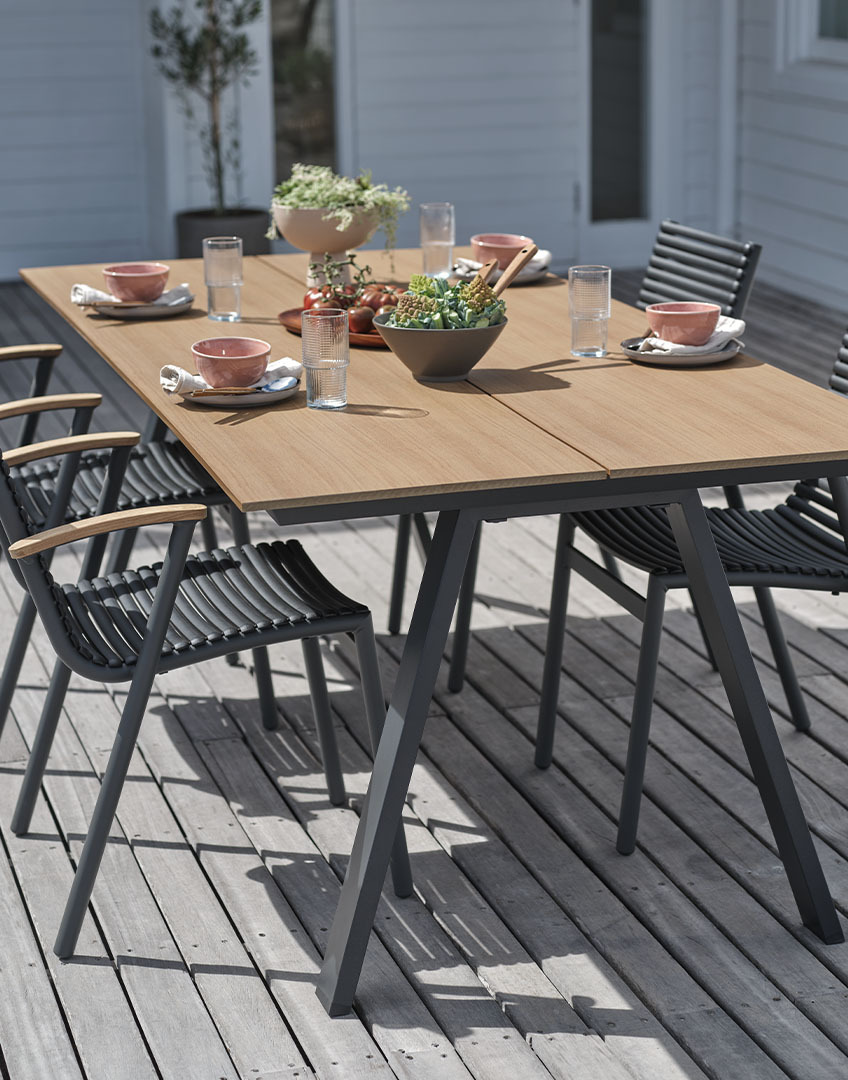 Vonkajší stôl s doskou z umelého drevo a stohovateľnými plastovými stoličkami s opierkami z recyklovaného tíkového dreva