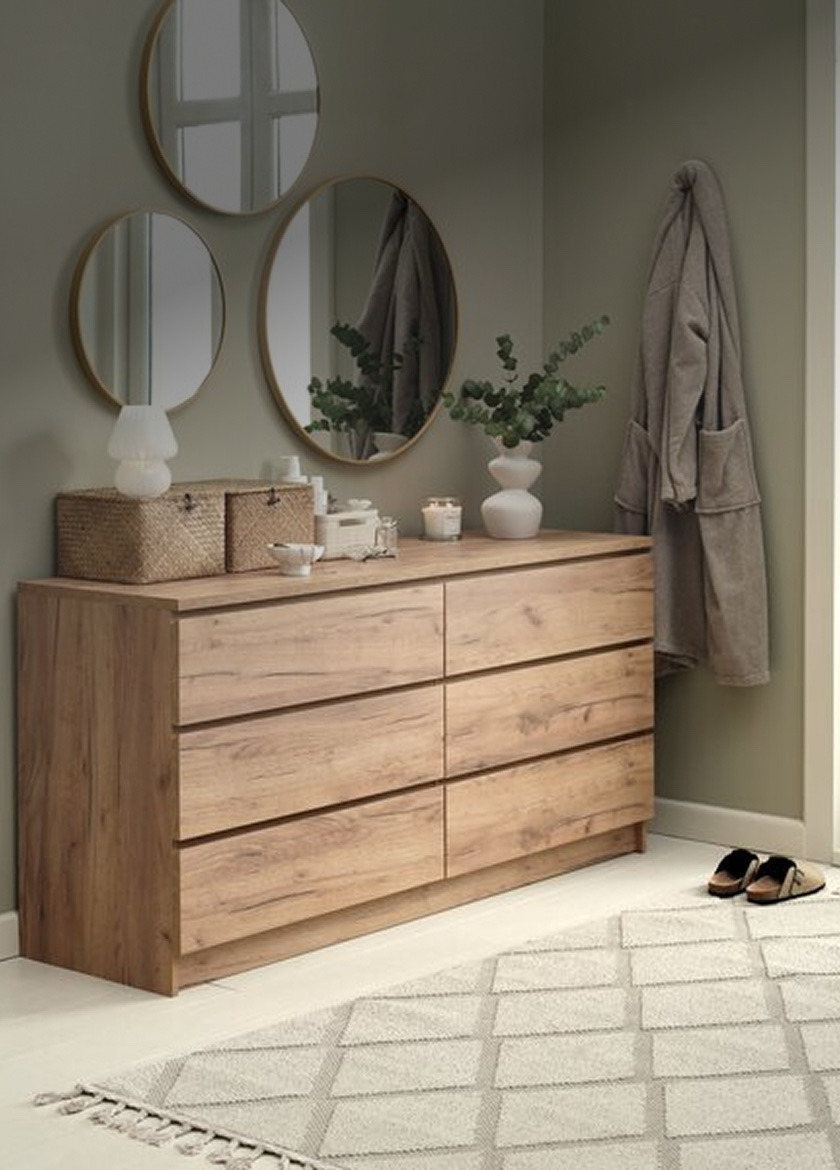 Wood-finish six-drawer chest of drawers below three round mirrors, styled with woven baskets, candles, and a vase of eucalyptus.