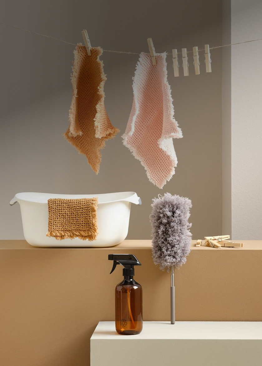 Pink and tan waffle-knit cloths hanging from clothespins above a wash basin, spray bottle, and duster.