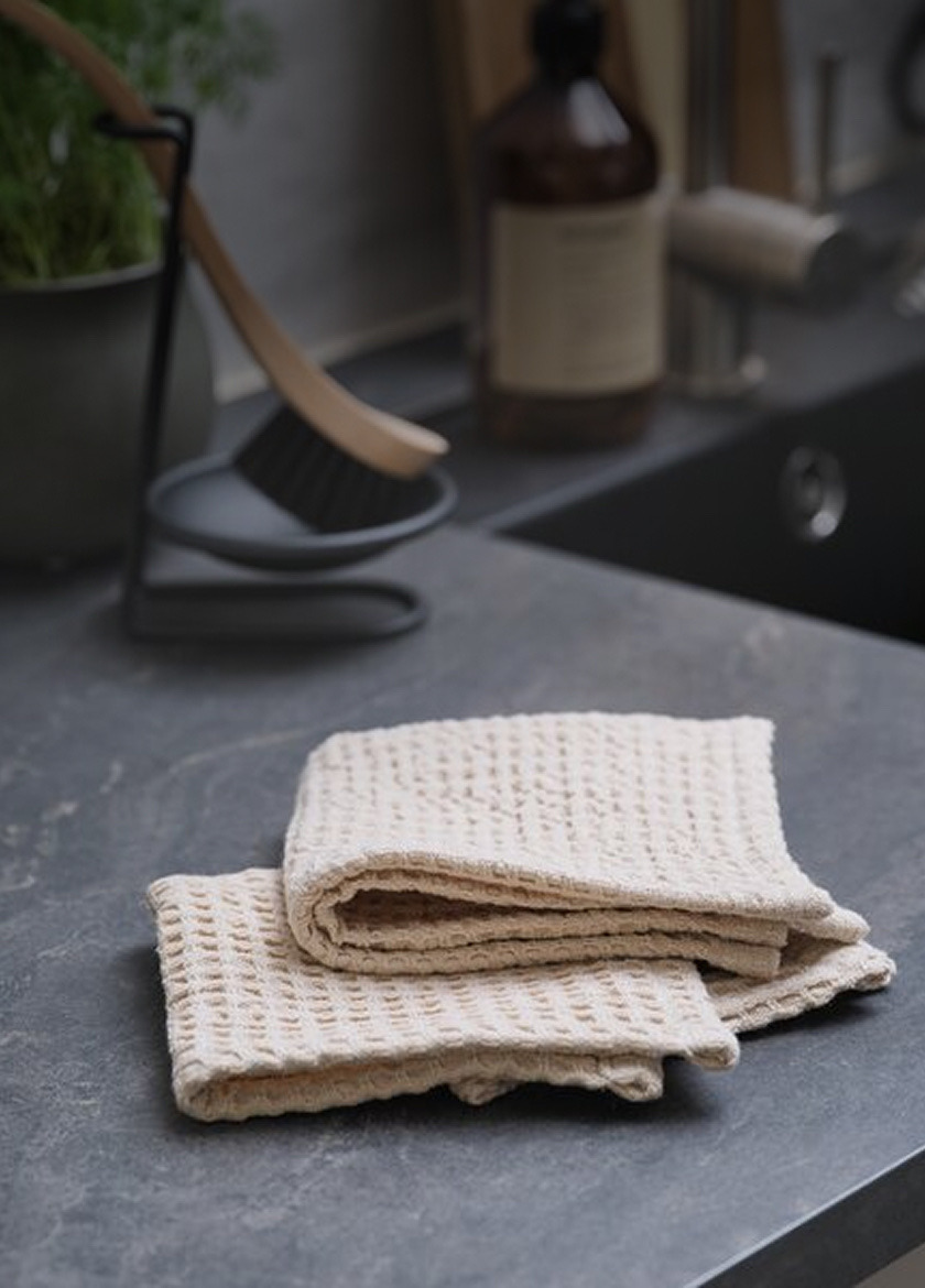 Folded beige waffle-knit cloths on a dark countertop, beside a cleaning brush stand and a bottle.