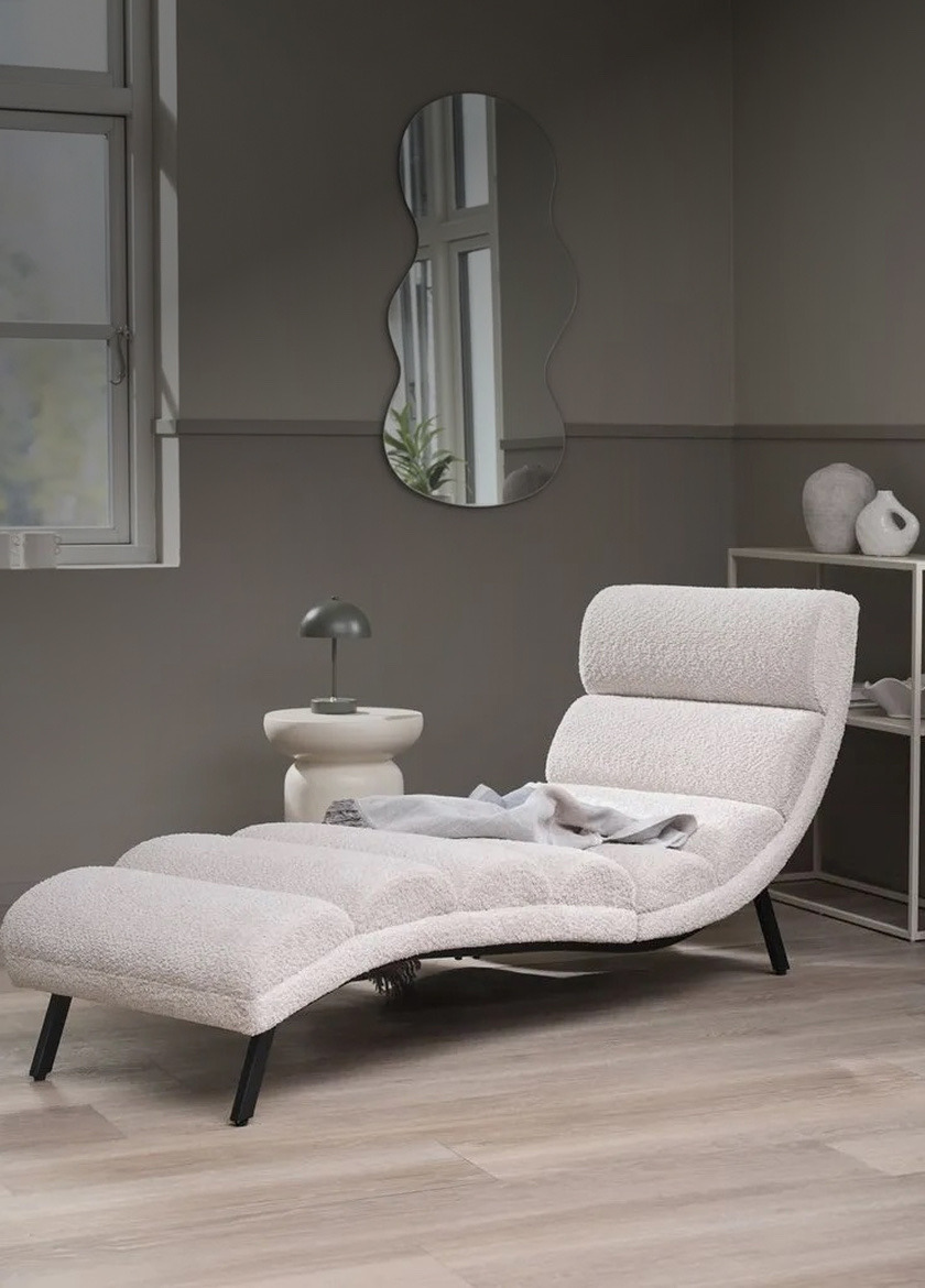 Daybeds White bouclé curved daybed chaise with a grey throw, beside a wavy wall mirror, a round side table, and a shelving unit.