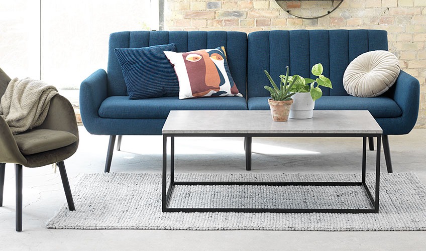 Living room with DOKKEDAL coffee table and HARNDRUP sofabed and UDSBJERG armchair Living room with coffee table, sofabed with cushions and armchair with throw