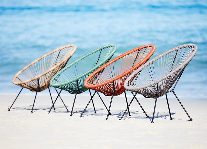 Four garden lounge chairs in different colours on a beach 