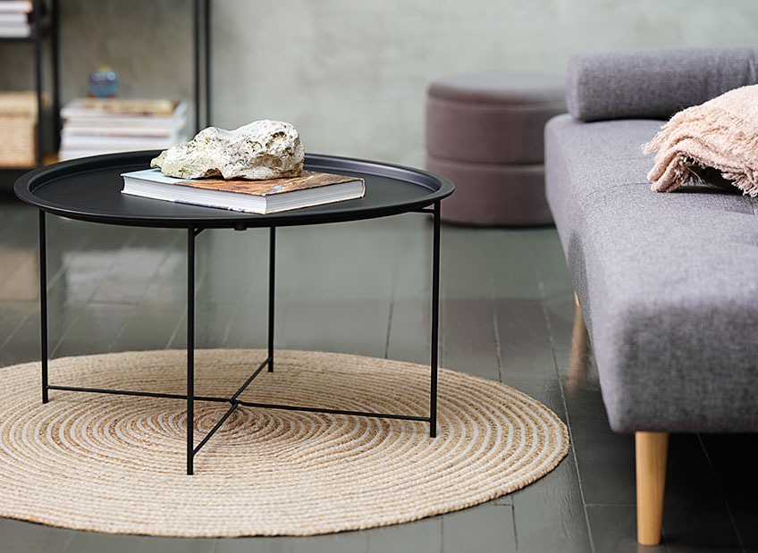 A coffee table on a circular rug in front of a sofa 