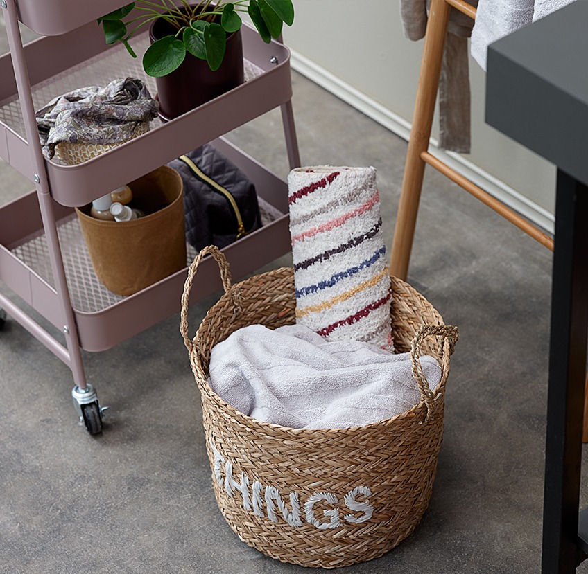 KANSTRUP trolley with bathroom accessories and ARVE basket with IRSTA bath mat Bathroom accessories on a trolley next to a wicker storage basket with towels and a bath mat in it