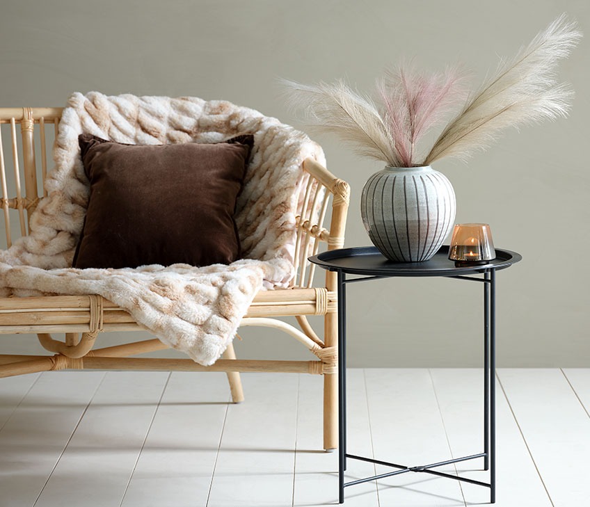Sofa with throw in fake fur and brown cushion. Black end table with vase and tealight holder