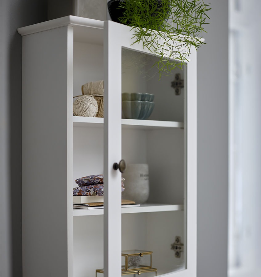White wall cabinet with glass front displaying decorative items 