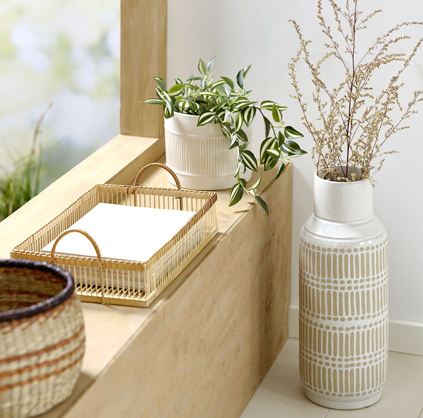 Vysoká váza vedľa parapety s podnosom z bambusu a bielym podnosom s umelou rastlinou
