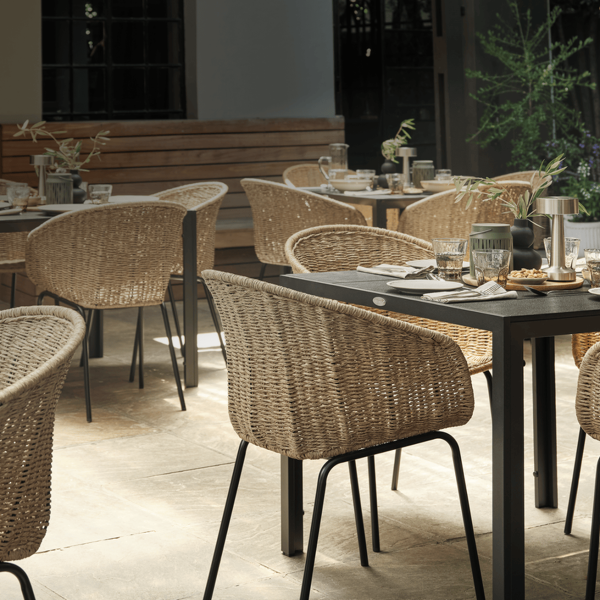 Food and beverage guides Outdoor garden dining terrace with wicker chairs around dark tables set for a meal, surrounded by greenery and warm lighting.