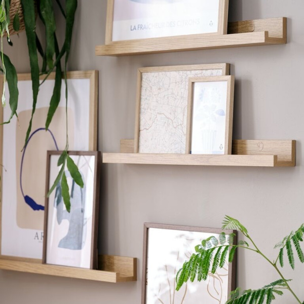 Oak picture ledge shelves mounted at staggered heights, displaying framed art prints and trailing potted plants.