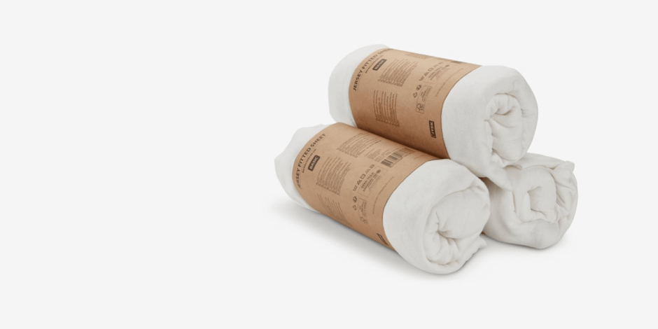 Two rolled white jersey fitted sheets wrapped in kraft paper packaging bands, shown against a plain light grey background.
