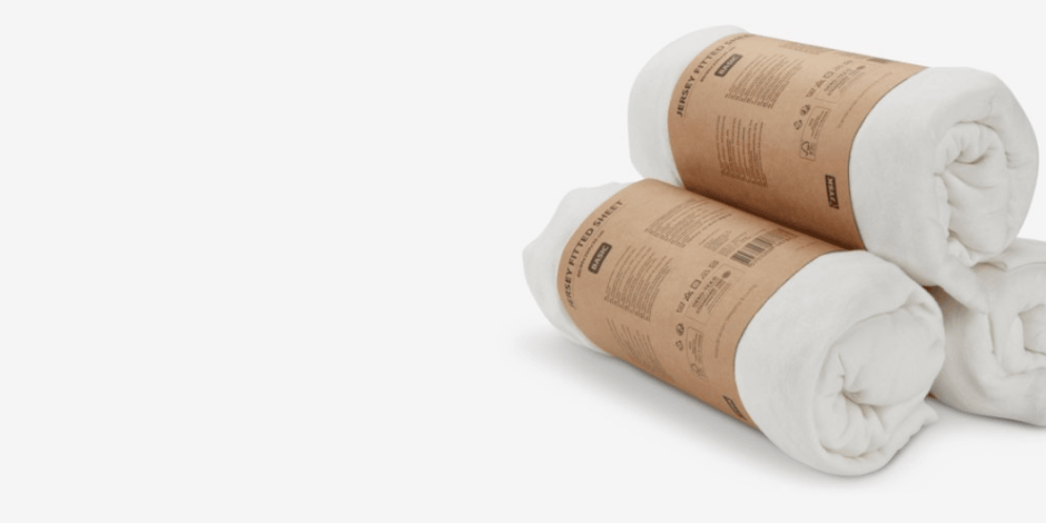 Two rolled white jersey fitted sheets wrapped in kraft paper packaging bands, shown against a plain light grey background.