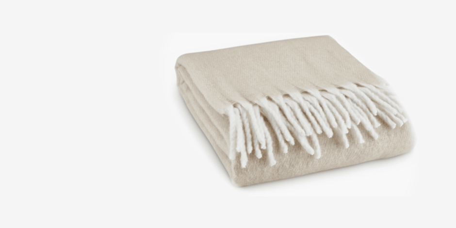 Throws Folded beige knit throw blanket with a fringed edge, shown against a plain white background.