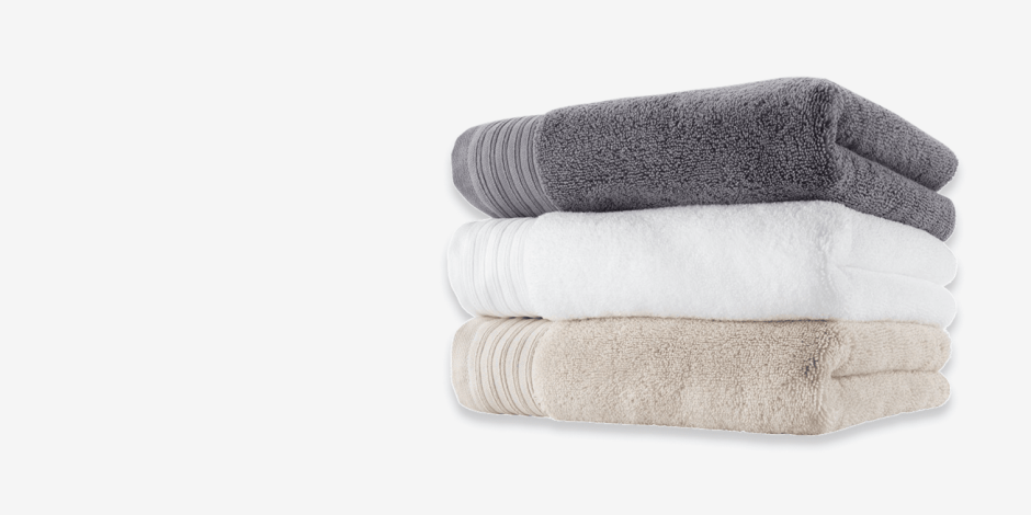 Stack of folded bath towels in grey, white, and beige, shown against a plain light background.