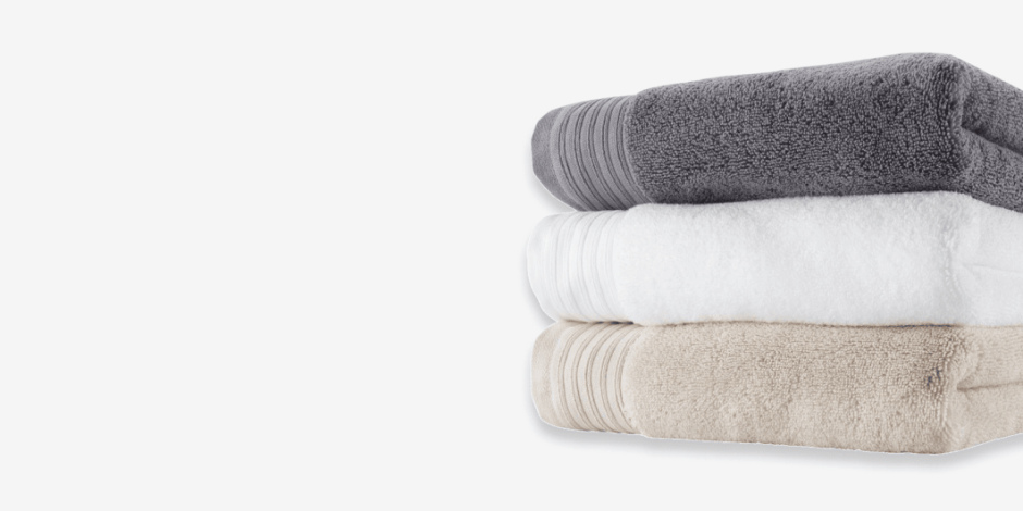 Stack of folded bath towels in grey, white, and beige, shown against a plain light background.