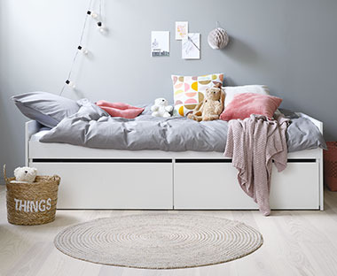 Biela detská posteľ so sivými obliečkami a farebnými ozdobnými vankúšmi