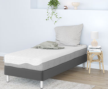 Biely matrac na sivom posteľovom ráme so sivým vaknúšom