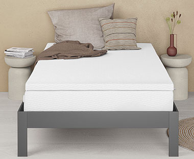 Biely matrac na sivom kovovom posteľovom ráme so sivými ozdobnými vankúšmi